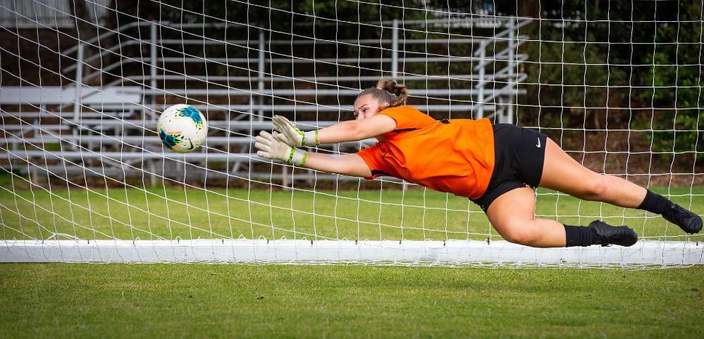 A soccer player dives for a ball in front of a soccer net. Photo: Paul Jones