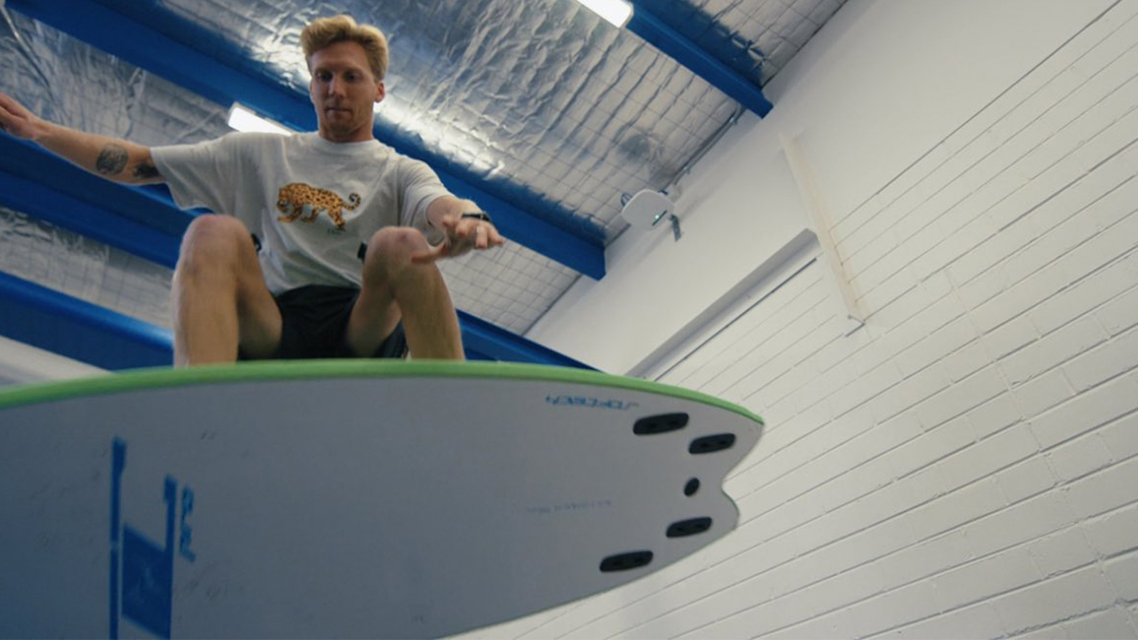 Brett Connellan is in an exercise lab performing an aerial on a surfboard.
