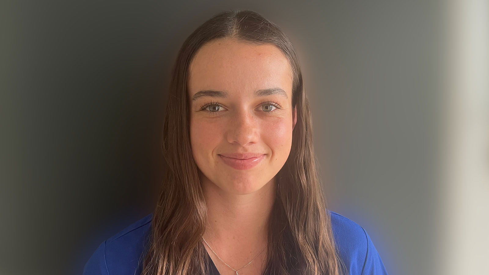 A UOW nursing student is standing against a plain wall smiling.