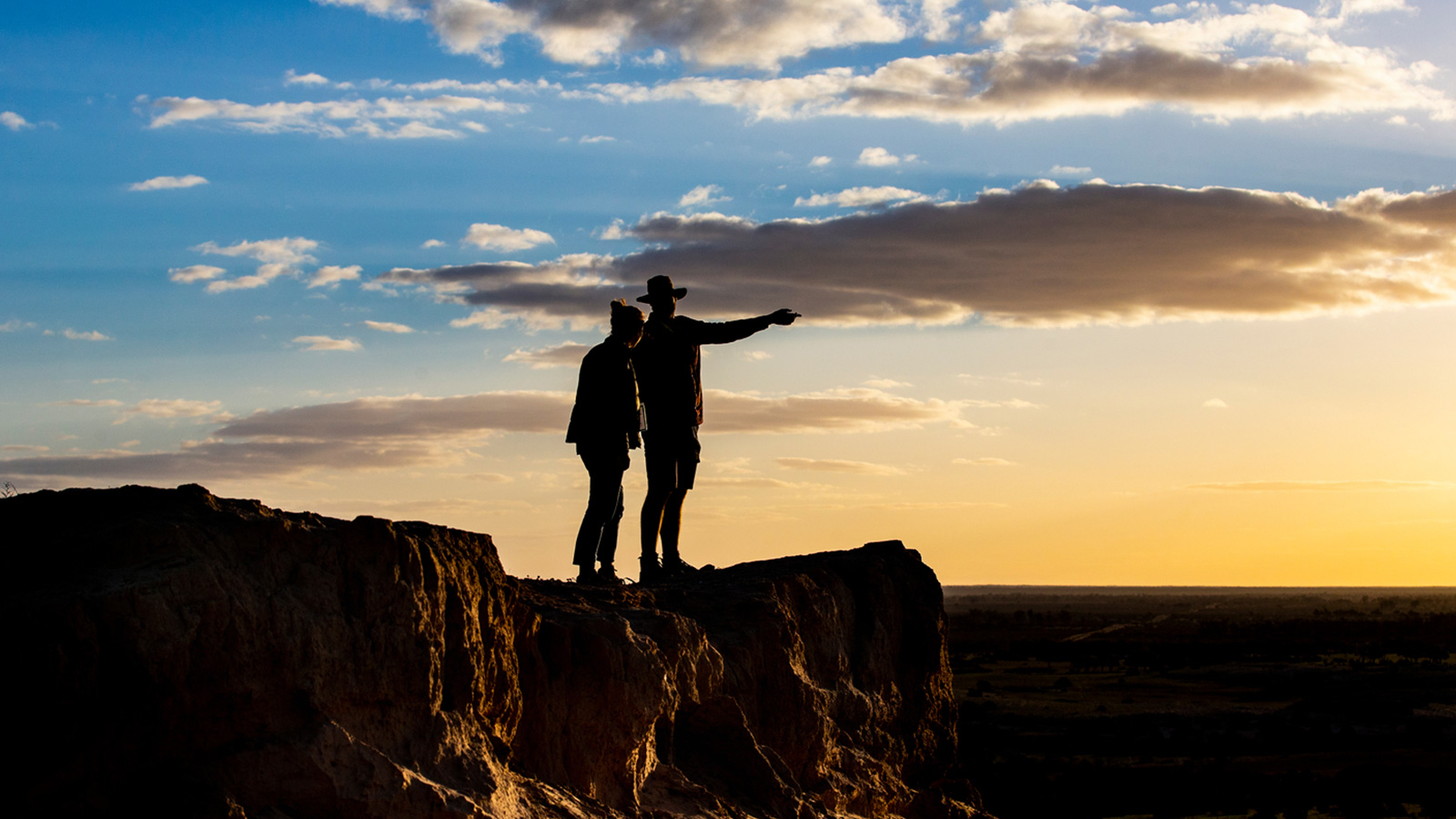 A man and a woman are standing atop a sand dune in the Australian desert