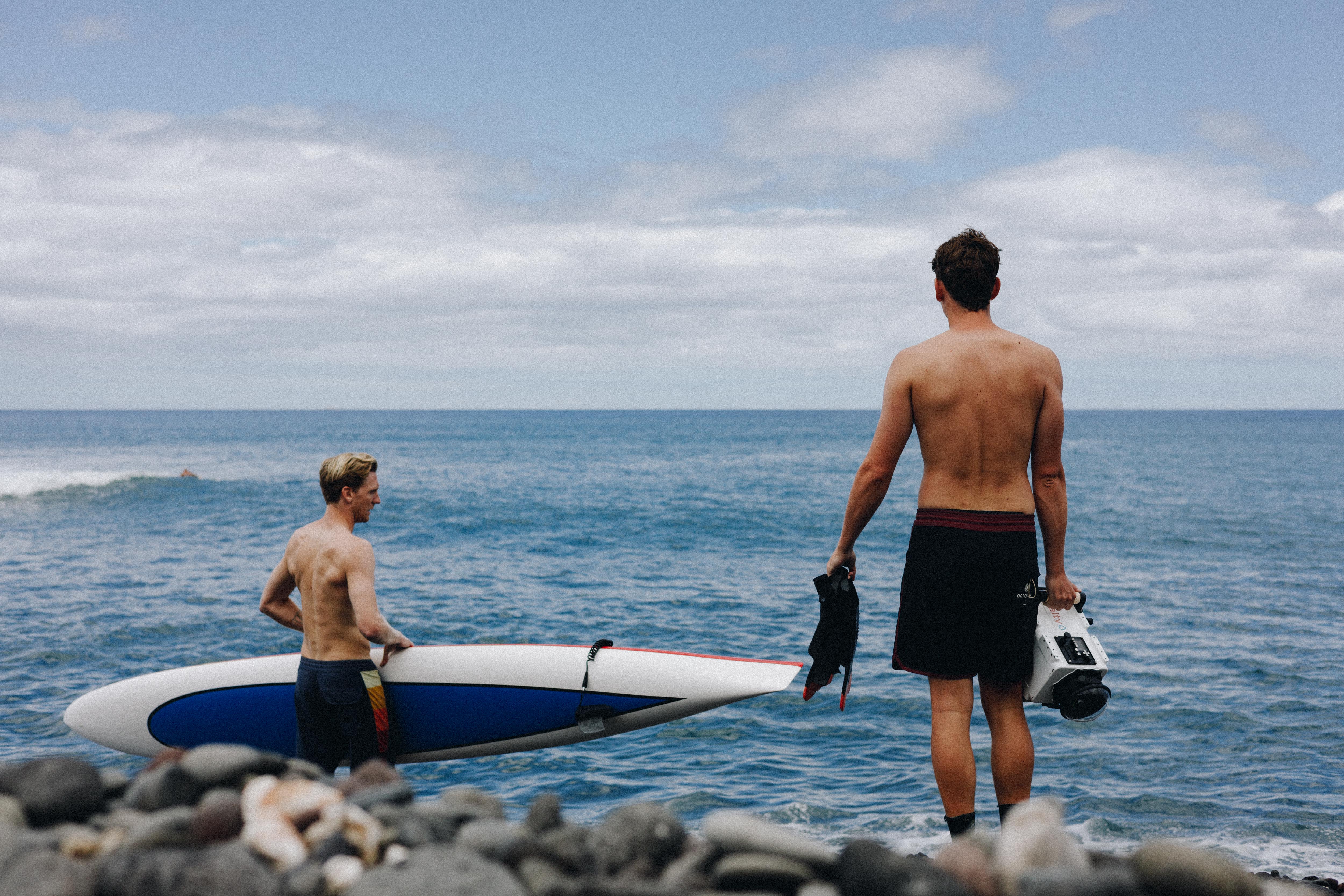 Brett Connellan is standing in the ocean with a large paddleboard. A man is on his right holding a navigation device.