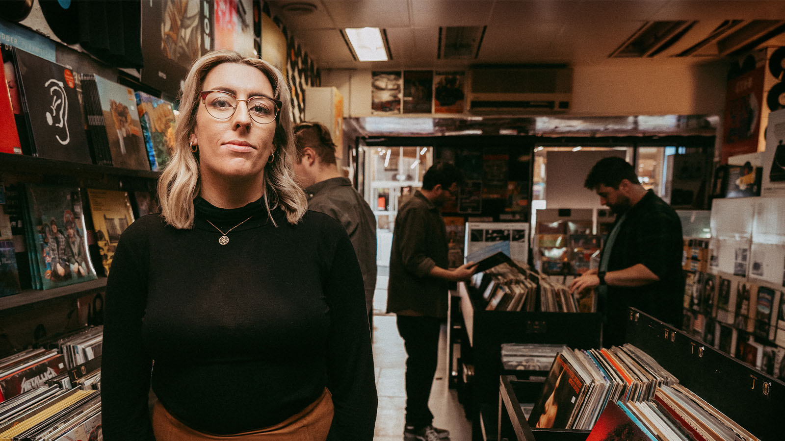 A woman is standing in a record store while three men browse records behind her