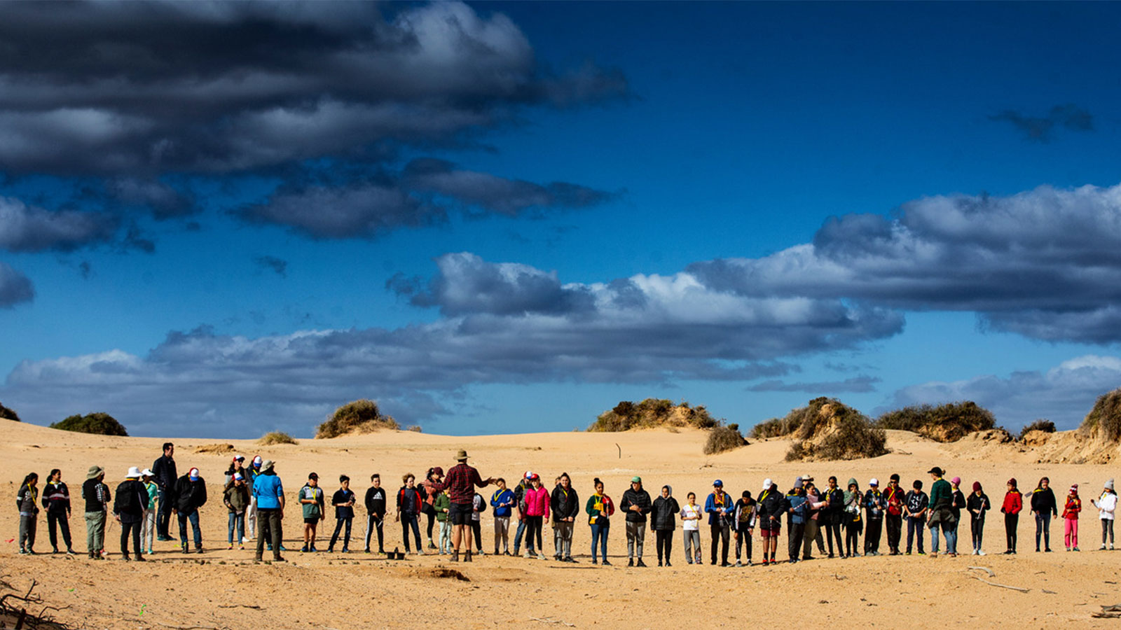 A line of school children standing in the desert learning from a teacher