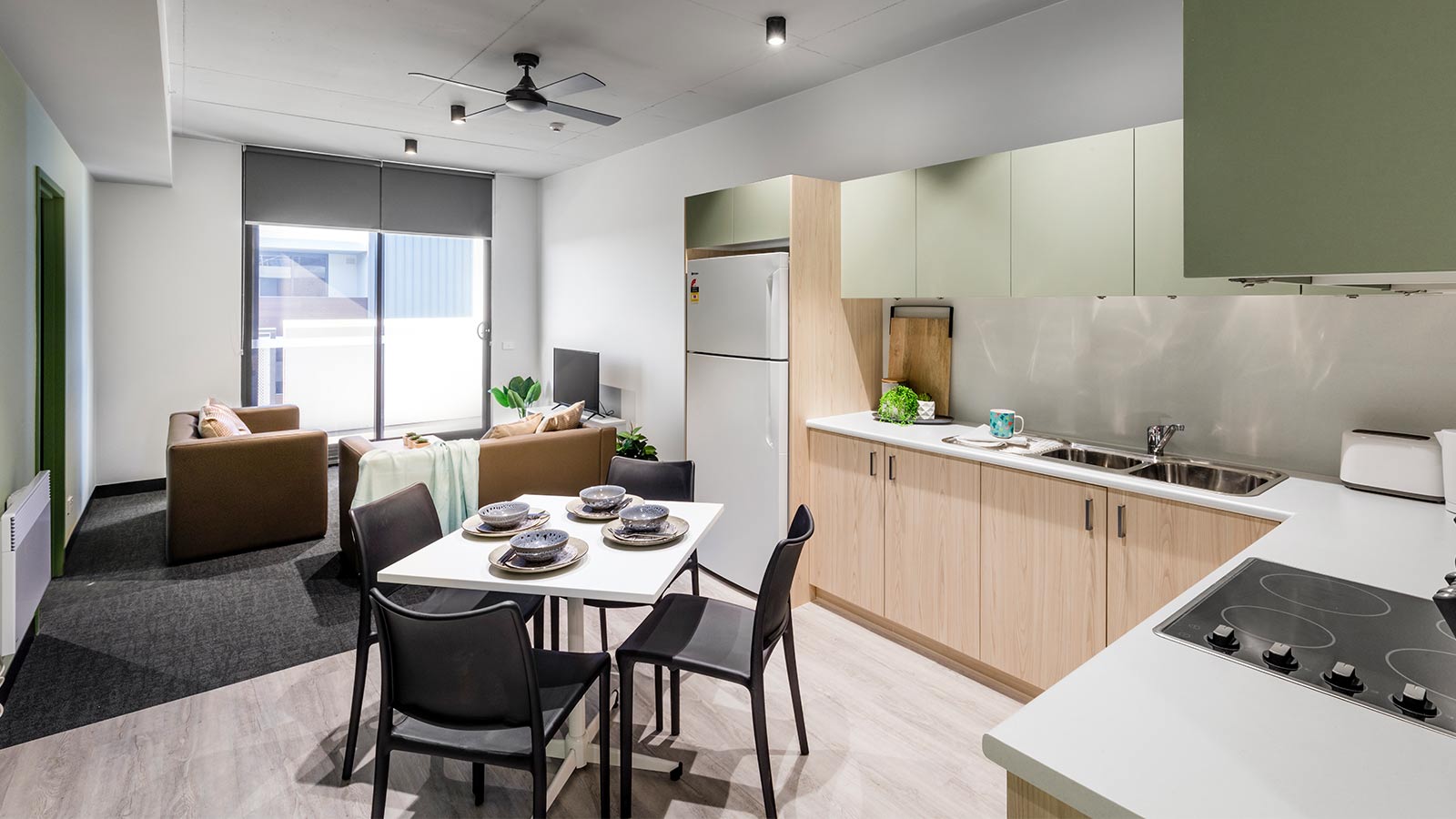 The inside of a UOW accommodation unit. There is a kitchen with green cabinets, a four seated dining table and two small lounges.