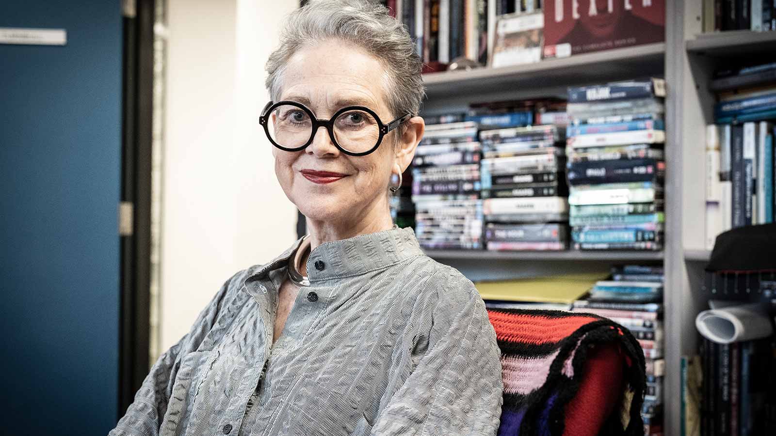 Sue Turnbull has pale skin and short, light hair. She is standing in front of a book shelf covered in crime books and films.