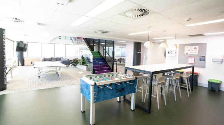 A open area with a stair case, grey lounge, while table and a Foosball table.