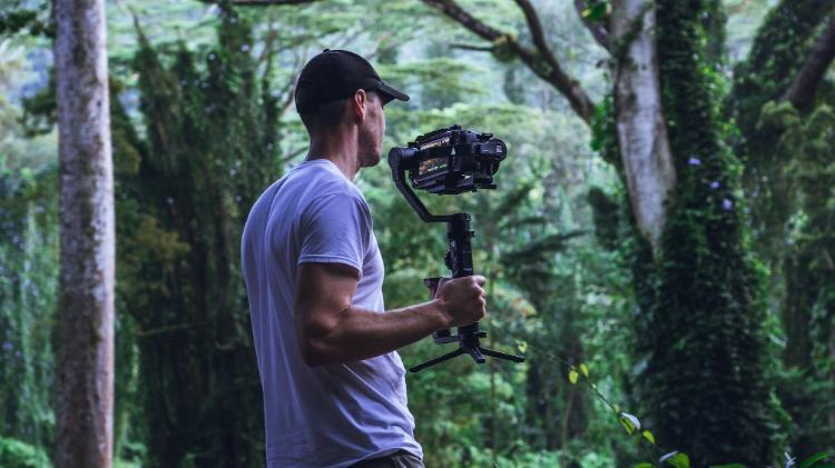 A man wearing a cap and t-shirt filming in a forest