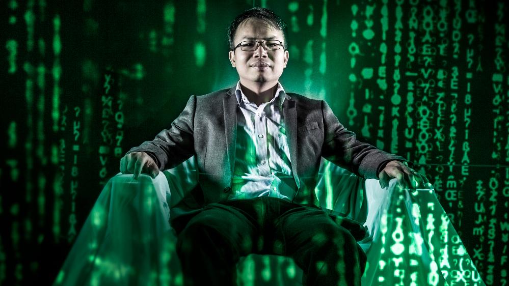 Photo shows, data mining expert, Hoa Dam sit on chair surrounded by falling green data