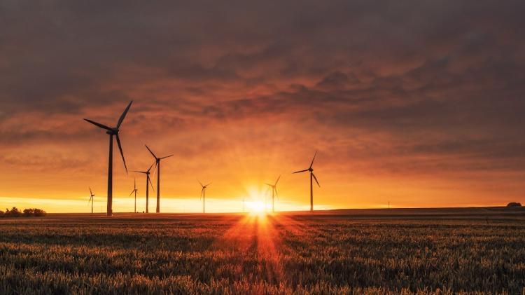 Wind mills in a grassy field with the sun setting in the background