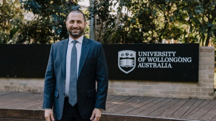 Adam Malouf COO standing outside and in front of the University of Wollongong sign..