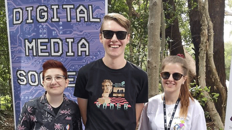 three students standing in front of a Digital media society banner 