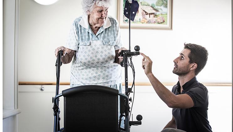 A UOW rehabilitation and gerontology graduate helps an elderly woman on a walking frame