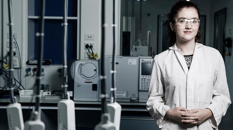 A UOW science research student stands in a laboratory wearing  a lab coat