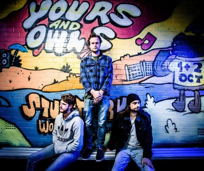 Three young men posing for a photo in front of a mural that says 