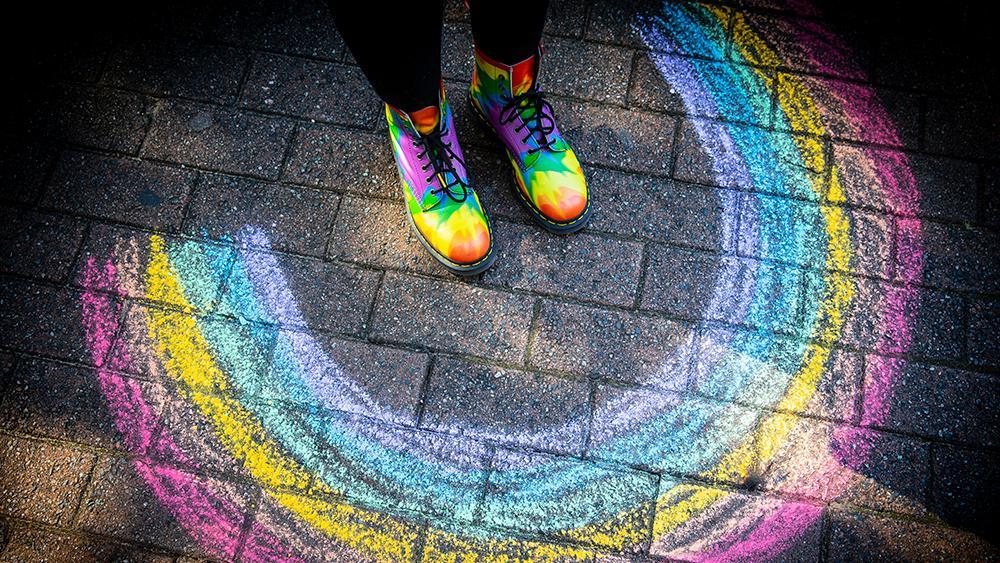 Colourful shoes standing next to a rainbow drawn in chalk on the ground