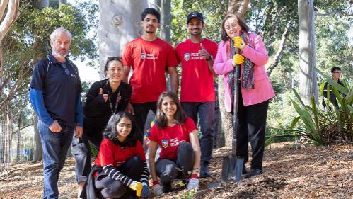 UOW Vice-Chancellor, Professor Patricia Davidson with the UOW Pulse team as the plant trees. The team wears red t-shirts with UOW Pulse branding.