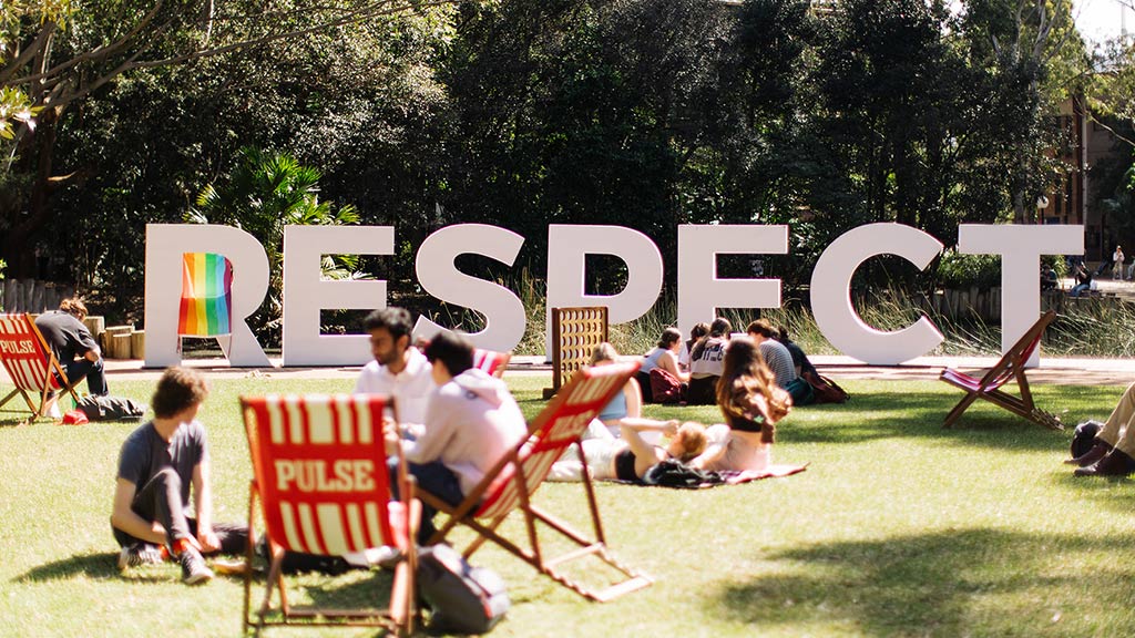 The white UOW RESPECT signage is displayed in front of the Duck Pond. Students are visible sitting on the Duck Pond lawn in PULSE deck chairs.