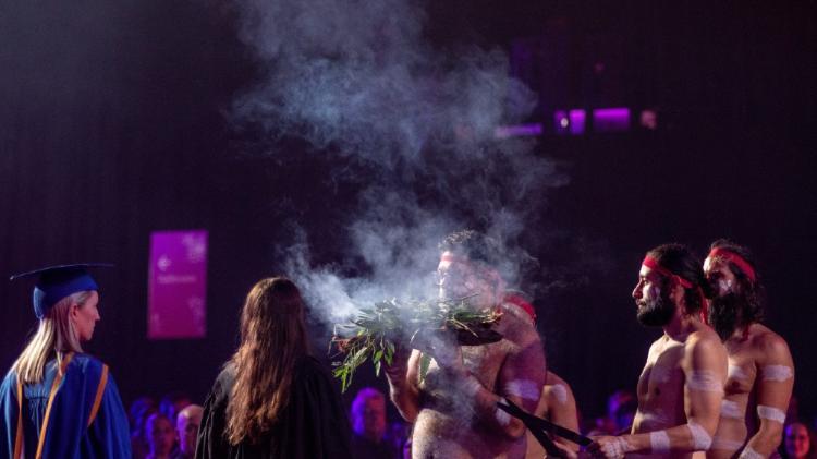 Smoking Ceremony at a UOW graduation ceremony. Graduate with blue gown standing at the side.