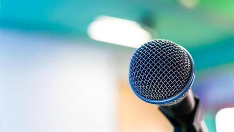 Close-up of a microphone against a softly blurred background, capturing its textured mesh and shiny trim.