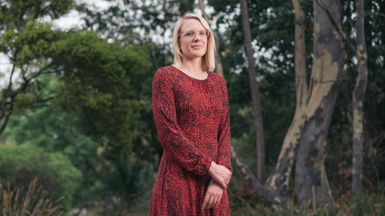 Lady in a red and black patterned dress standing in front of trees