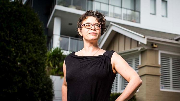 Dr Nicole Cook wearing a black dress and glasses standing in front of houses and departments.