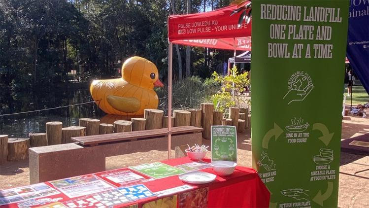 Stall table with a large green banner on the lift side. A large yellow inflatable duck sits in the bckground.