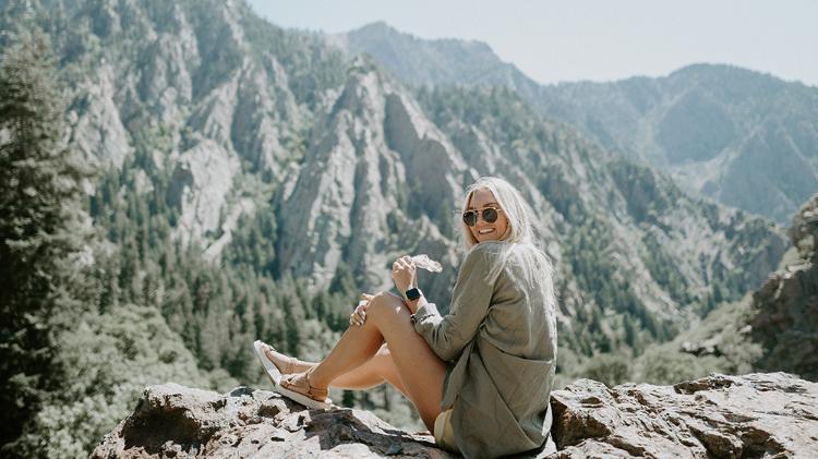 Girl wearing sunglasses sitting on mountain rocks