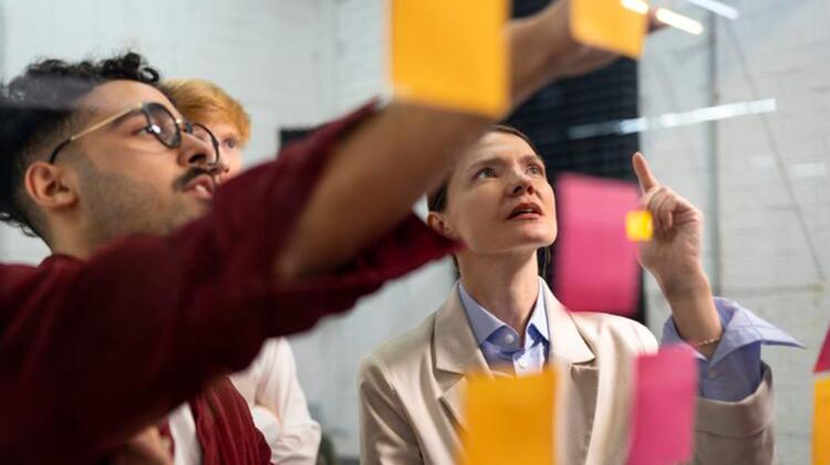 A group of professionals in a collaborative setting, engaging with colorful sticky notes on a glass board, brainstorming ideas.