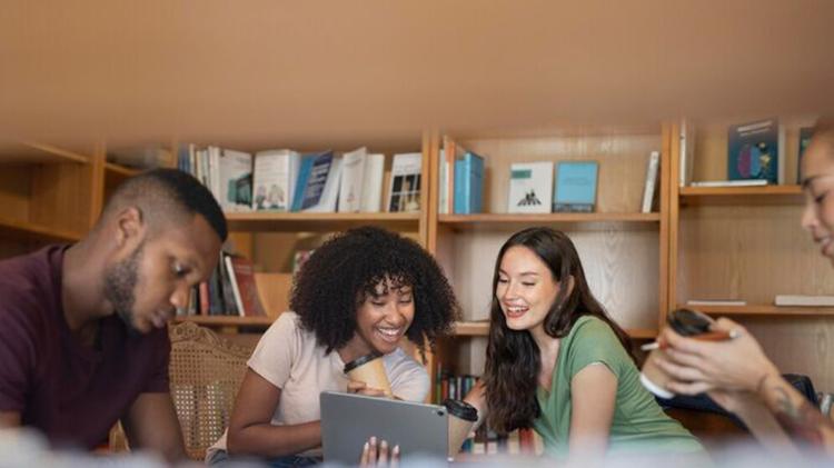 A group of people sitting in a room, looking at a phone together while surrounded by books and shelves.