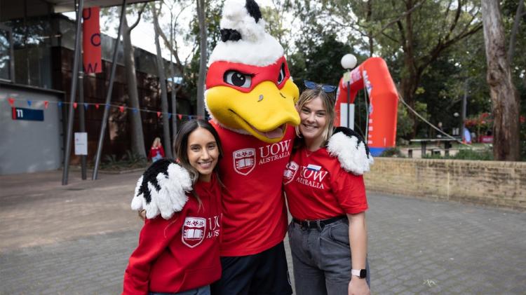 UOW Mascot duck, Bexter, hugging two people all wearing red UOW t-shirts