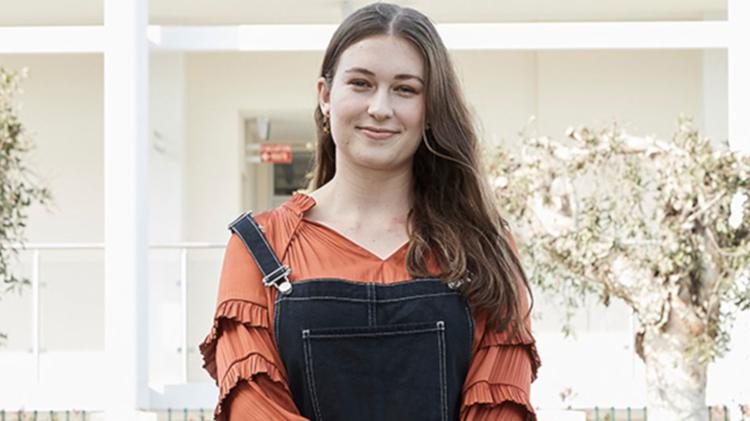 A student smiling wearing dark overalls with a orange shirt underneath
