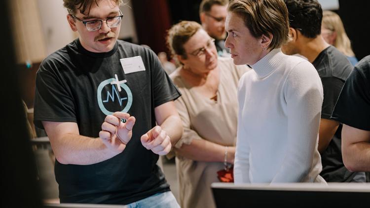 A group of people engages in discussion, with one person demonstrating something on a device, creating an interactive atmosphere.