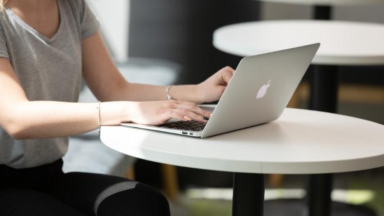 Person in grey t-shirt using a laptop on a white round table