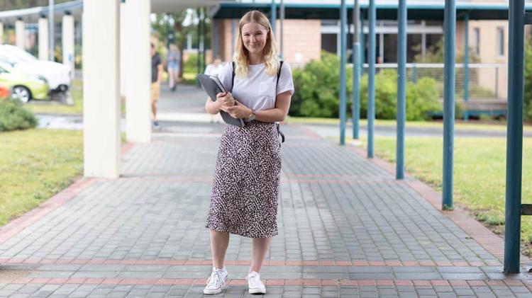 Female student holding books, standing on a path at Shoalhaven campus