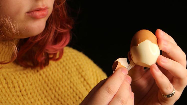 Close up of a woman in a mustard coloured jumper, peeling boiled egg