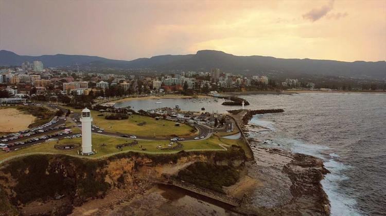 The city of Wollongong from a drones view. The image looks north-west from above the sea, visible are some of Wollongong's iconic landmarks, the lighthouse, Northbeach, Mt Kiera, Wollongong Harbour and the continental pools.