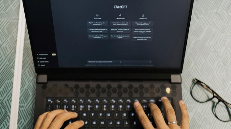 Fingers typing on a laptop with the ChatGPT homepage showing in Dark display view on the screen.