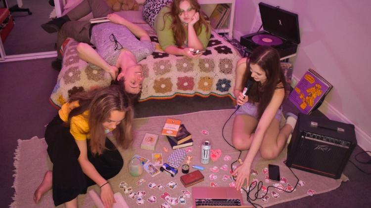 Four teenagers hanging out in a bedroom with a laptop and microphone