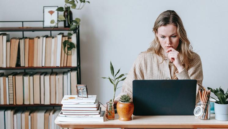 Woman sitting at desk looking down at computer, she has a bookshelf behind her