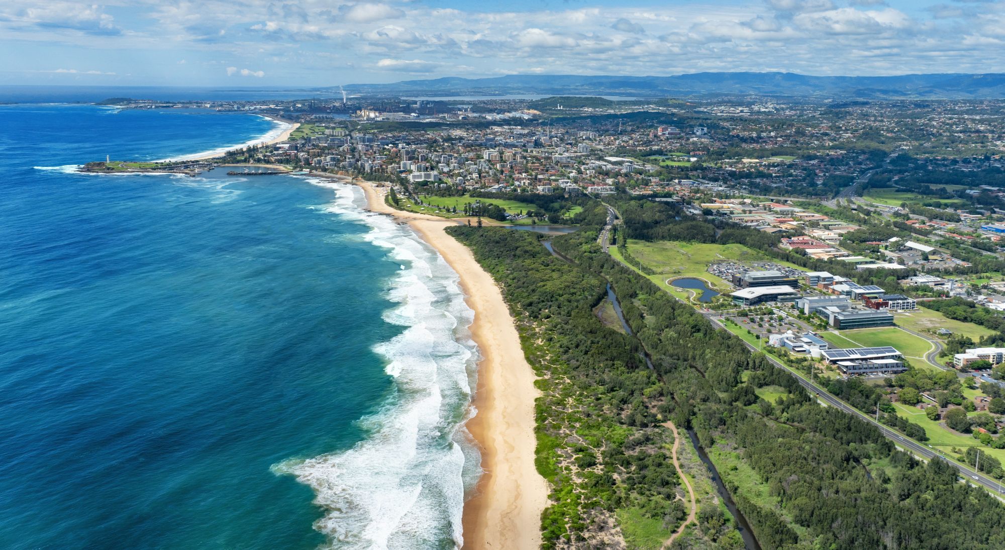 Aerial view of Wollongong coastline with beaches, ocean, and Innovation Campus buildings.