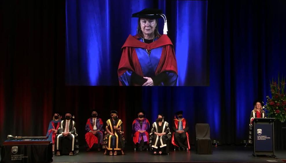 Professor Fiona Wood, pictured accepting her Doctor of Science during UOW's virtual graduation. The image shows Fiona projected on to a screen behind a group of people on stage.