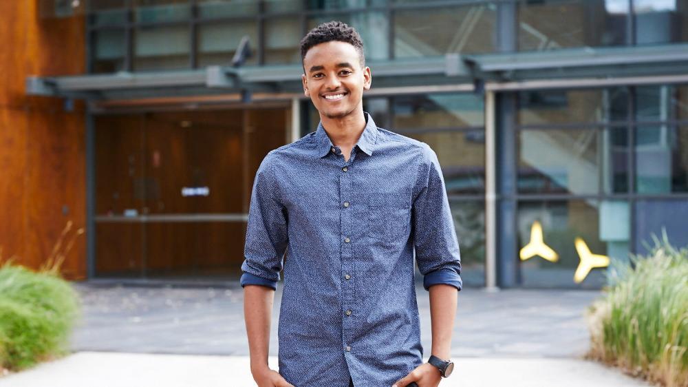 Teklemariam Mengistu stands in front of a building at UOW. He wears a blue shirt and is smiling. Photo: Tim Jones