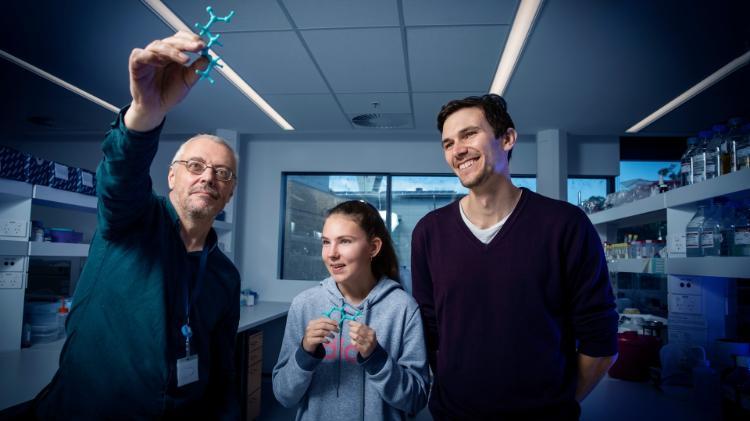 Associate Professor Aaron Oakley holds an example of the 3D chemistry model. Next to him is student Karlee Symonds and Dr Patrick McClosker, who helps Karlee in the lab. They are situated in a laboratory and are all smiling. Photo: Paul Jones
