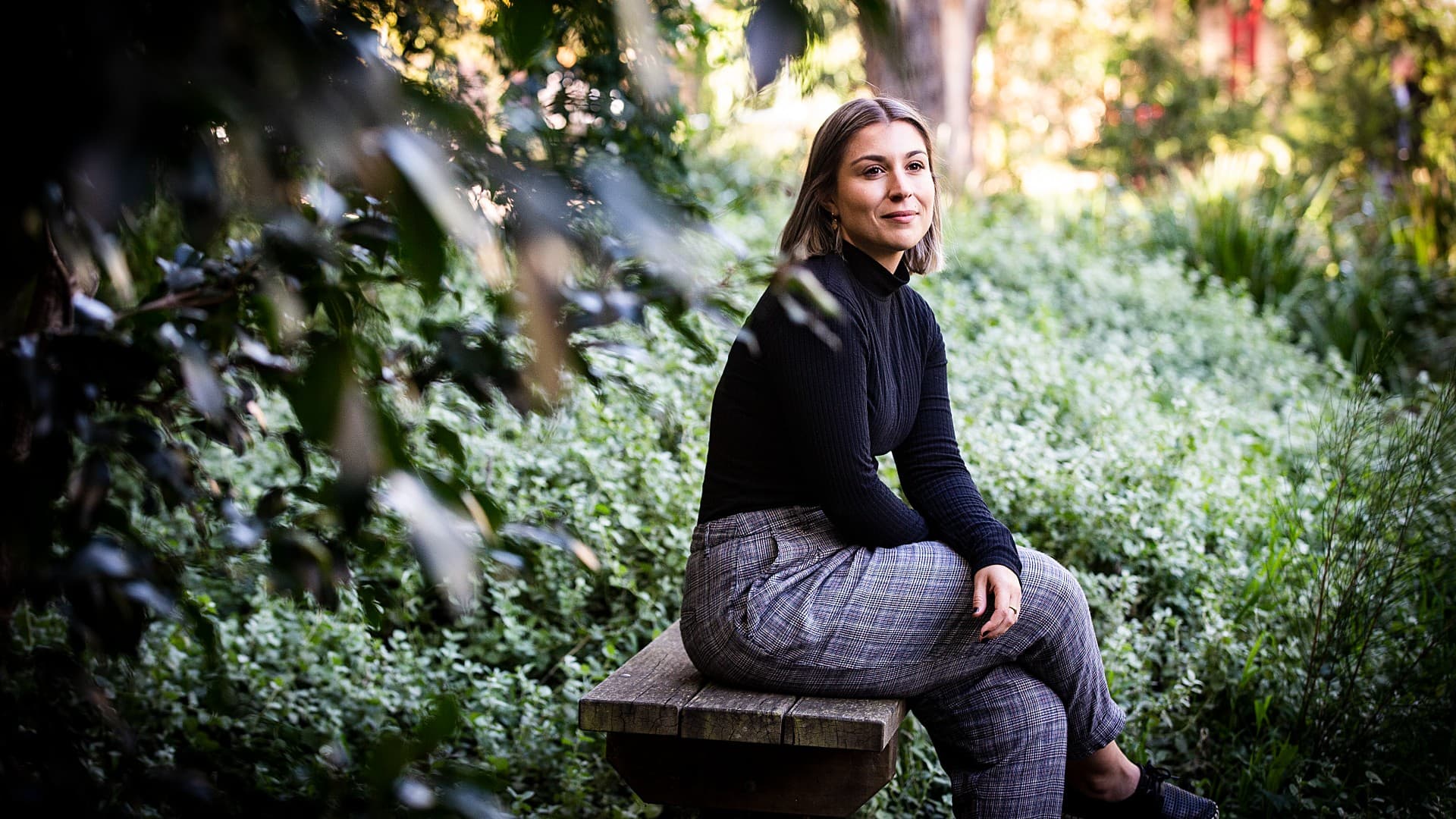 An image of PhD student Alixandra Risi sitting on a bench surrounded by trees. Photo: Paul Jones