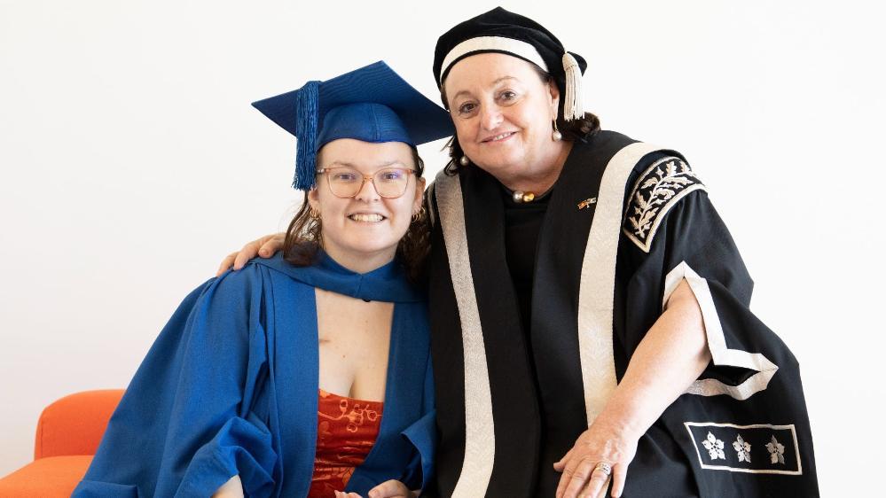 UOW graduate Catie Brown hugs UOW Vice-Chancellor Professor Patricia Davidson. Professor Davidson wears a black graduation gown and cap while Catie wears a blue gown and cap. Photo: Paul Jones