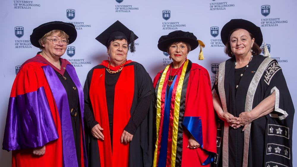Professor Eileen McLaughlin, Professor Kathy Clapham, Professor Bronwyn Fredericks and Professor Patricia Davidson in front of a media wall. They all wear graduation gowns and caps. Photo: Andy Zakeli