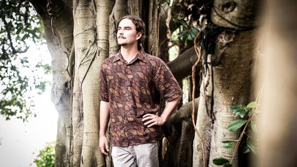 UOW student Charlie Gluskie stands next to a tree, surrounded by bush. Photo: Paul Jones