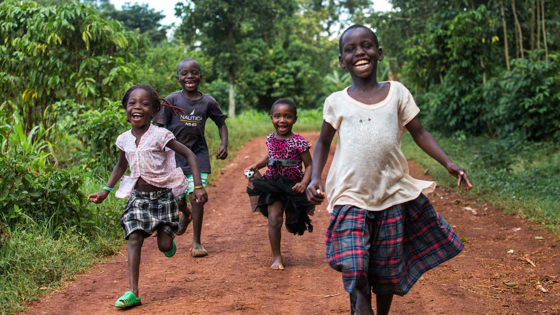 Four young African children run along a road smiling happily. Shutterstock