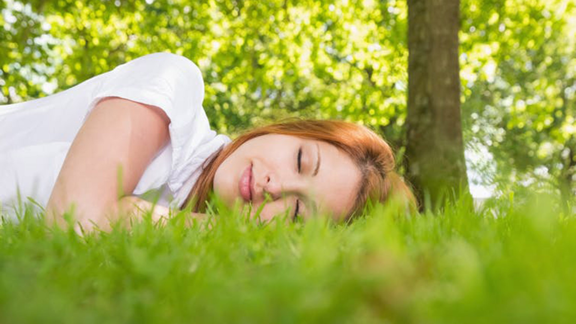 A young women sleeping on grass under a tree.