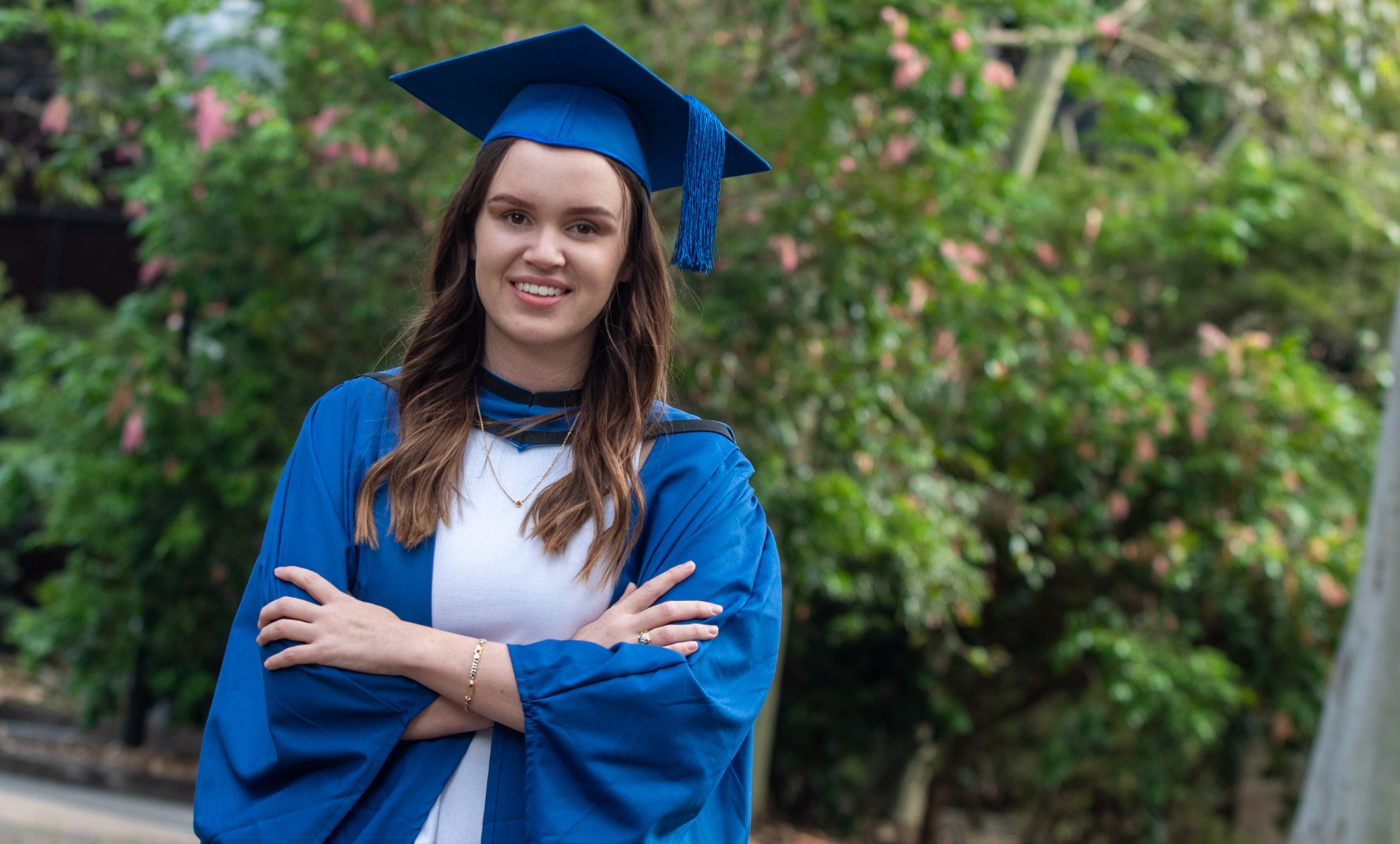 Ruby Evans wears a white dress and a blue gown and mortar board and smiles at the camera. Photo: Andy Zakeli